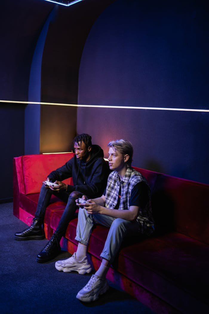 get-in-touch Two young men intently playing video games indoors on a stylish red sofa.